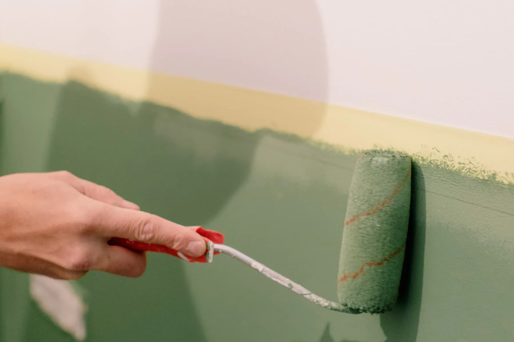 A hand rolls green paint up to a line of painter's tape.